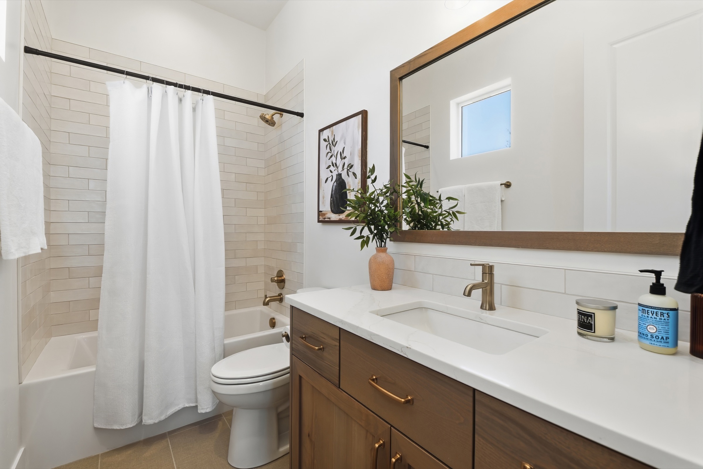 Bright secondary bathroom with a walnut vanity, brass fixtures, and warm wood accents
