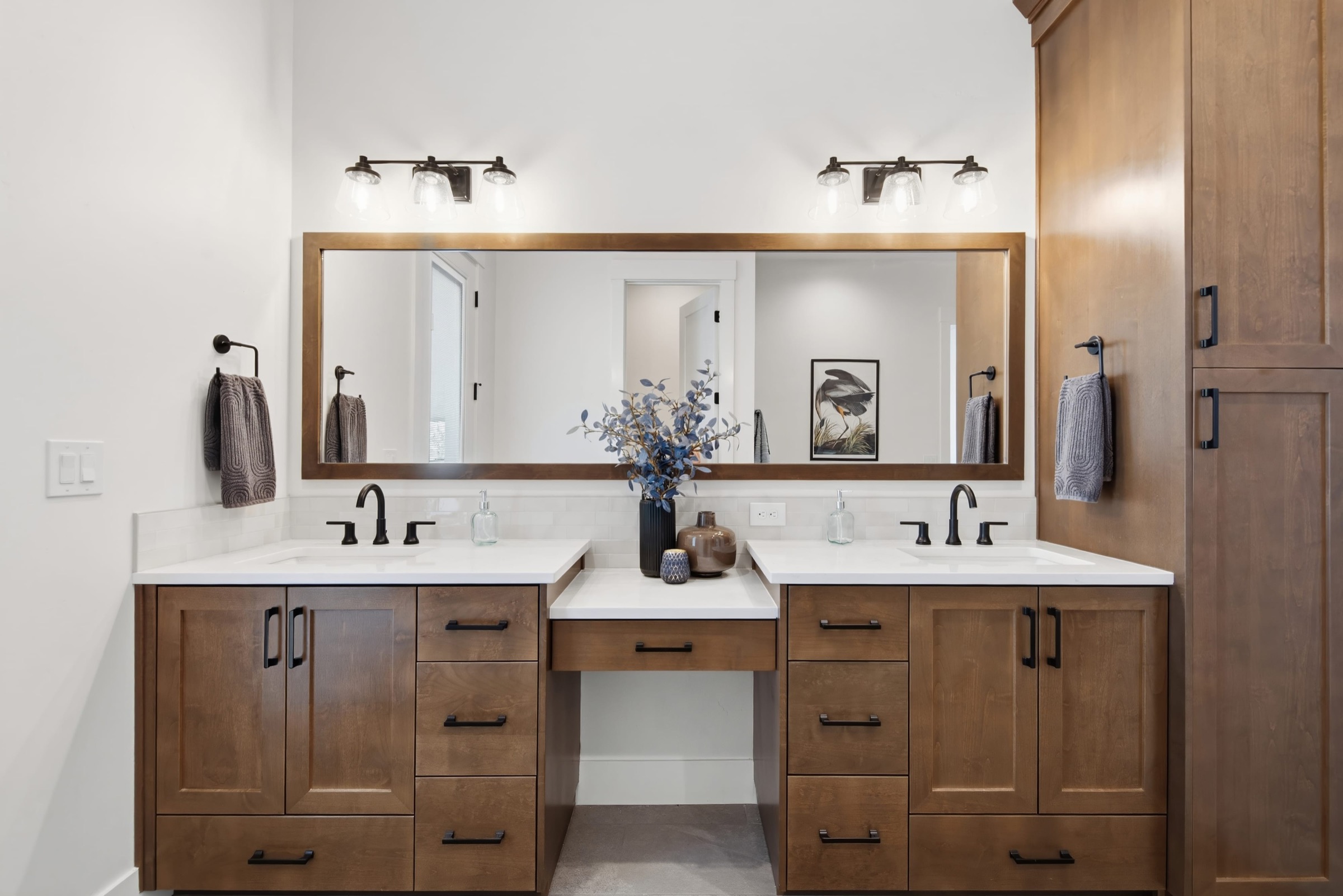 Custom walnut dressing vanity with a large wood-framed mirror and black fixtures