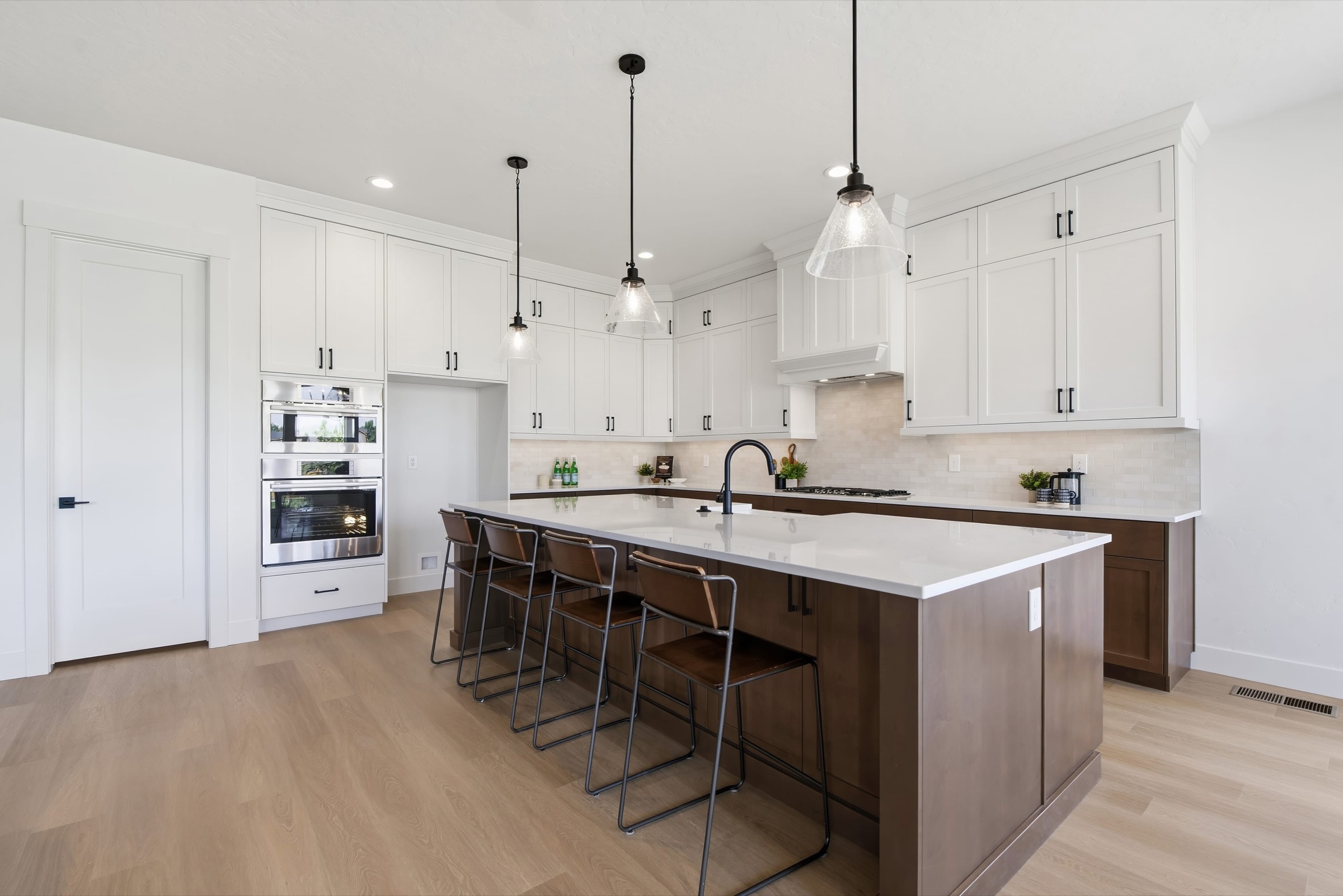 Open kitchen with white perimeter cabinetry, a walnut island, and black pendant lights