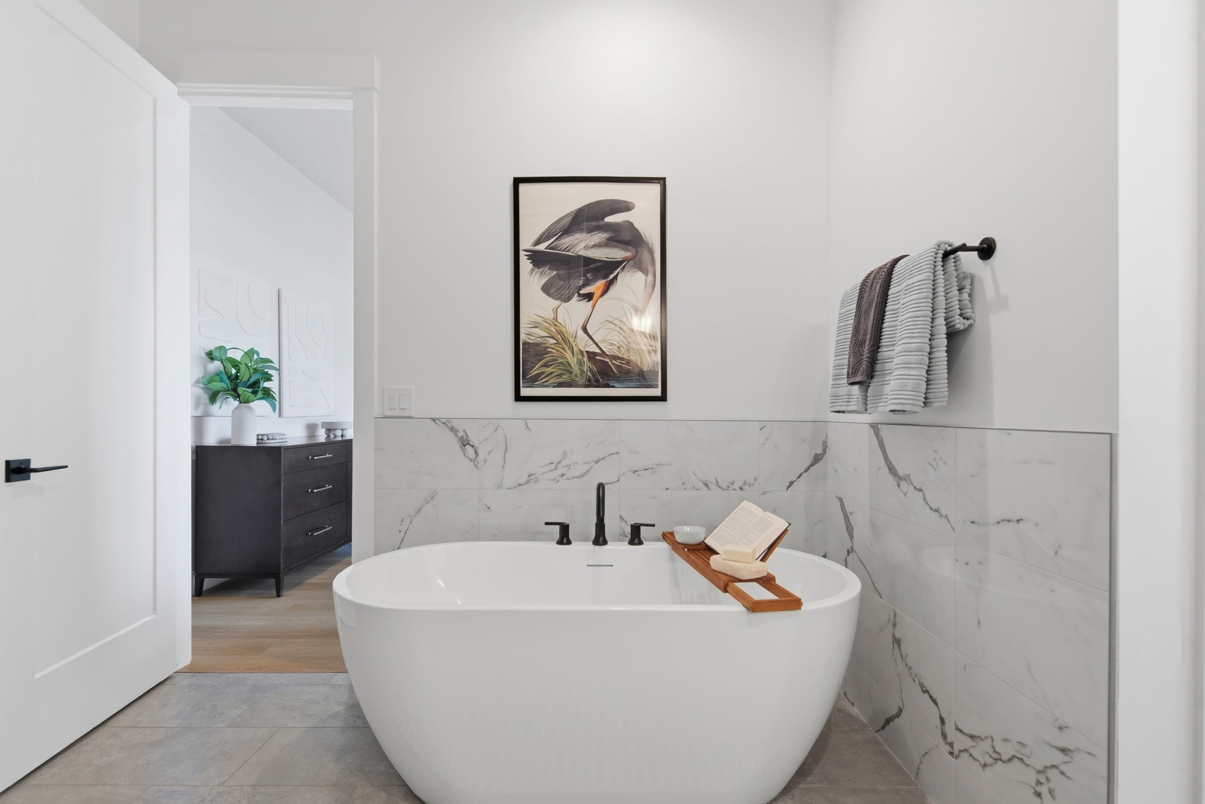 Freestanding soaking tub framed by marble-look tile and warm wood flooring